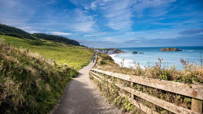 Coastal path running alongside sea with bright blue skies overhead
