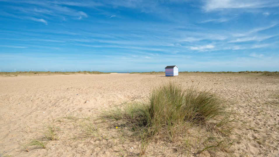 Small beach hut among sands and grassy patches at Great Yarmouth beach