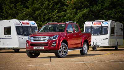 Red Isuzu tow truck parked in front of two caravans