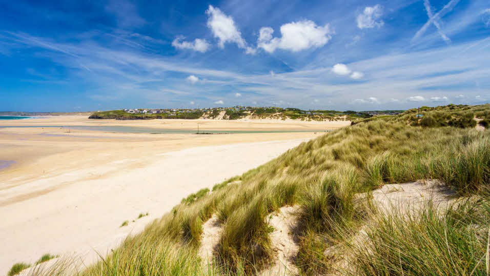 Grassy sand dunes at Porthkidney Beach, with clear blue skies and low tide