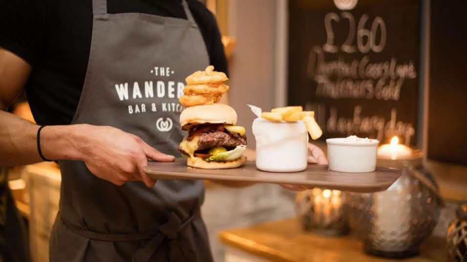 Man holding tray of burgers and chips at The Wanderer restaurant
